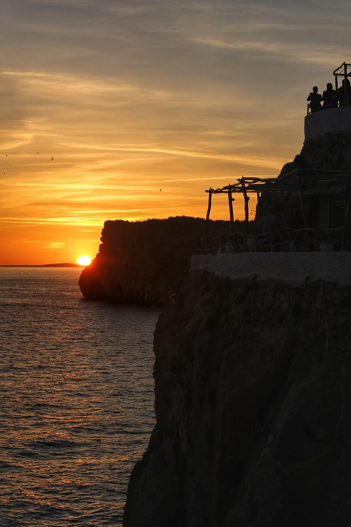 Sunset over the Menorcan coast at Cova d'en Xoroi, the golden-hour finish that west-coast boat trips from Ciutadella return into