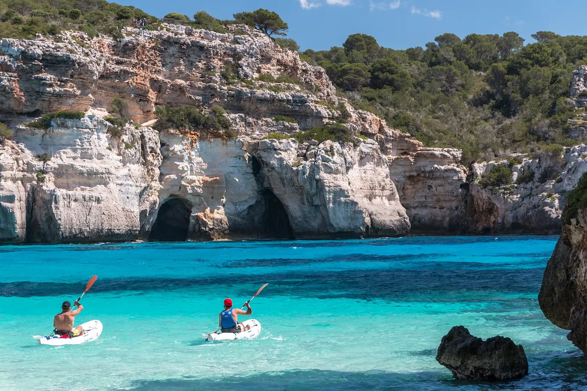 Two canoeists paddling the clear turquoise water near Cala Macarelleta in Menorca