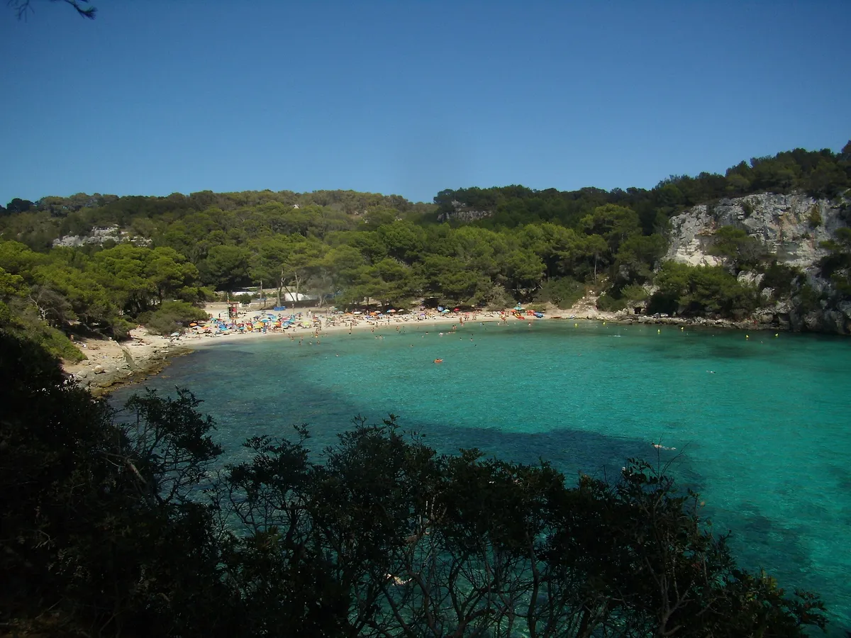 Cala Macarella beach full of summer umbrellas under white cliffs, Menorca - the arrival every route on this page is competing for