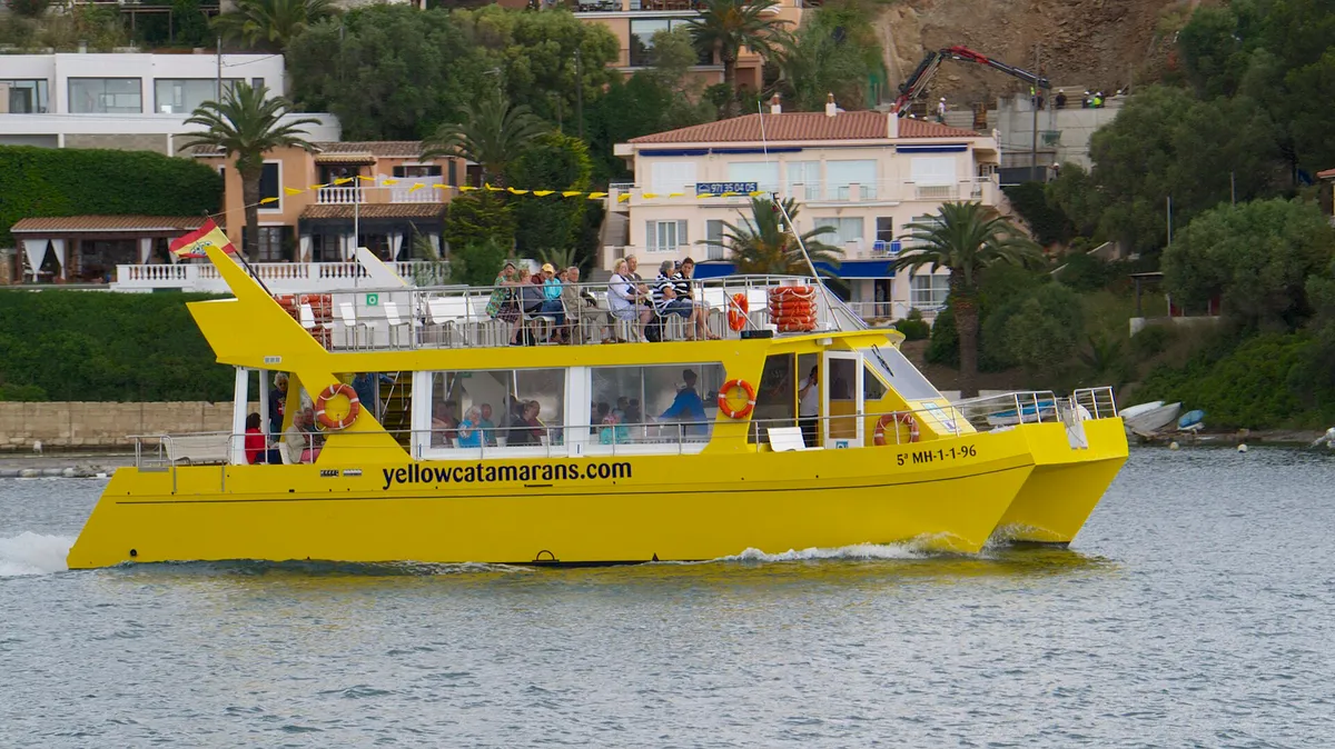 Yellow glass-bottomed catamaran carrying families on a harbour trip in Mahon, Menorca - the toddler-safe one-hour circuit