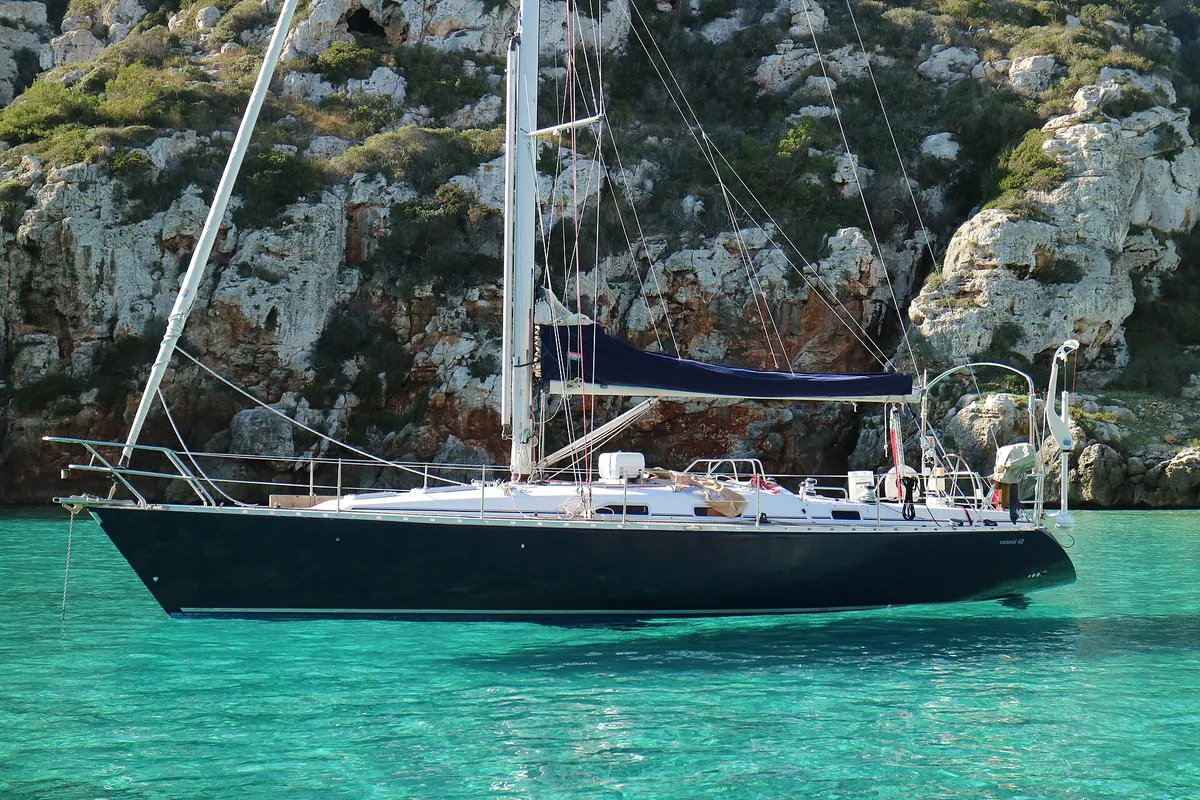 Sailing yacht at anchor off Menorca's south coast with full sun on deck, the exposure that decides the sunscreen factor for a boat trip
