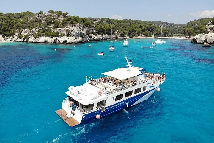 White motor boat anchored in a turquoise cove on the south coast of Menorca on a full-day boat trip with paella lunch from Ciutadella