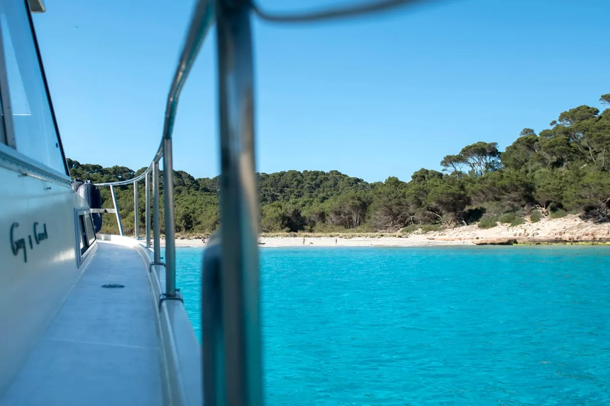 Boat full of travellers anchored in a turquoise cove on the 3.5 hour south coast boat excursion from Cala Galdana in Menorca