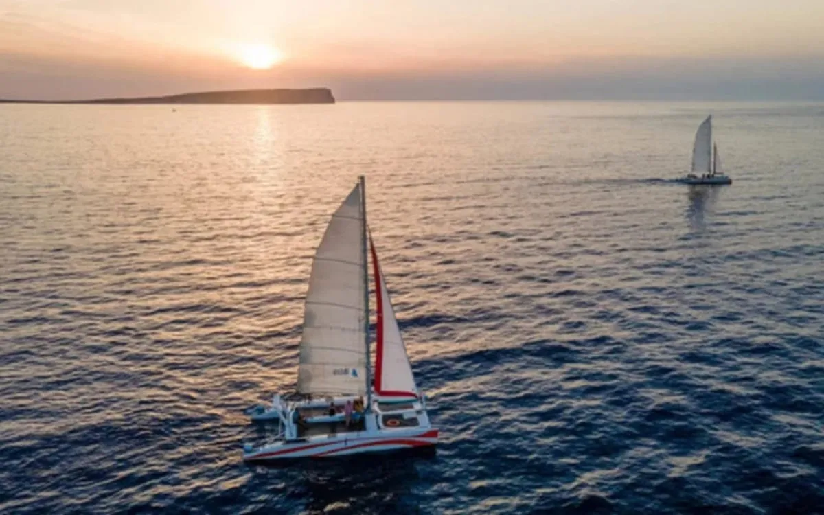 Catamaran sailing into the sunset off Fornells in Menorca with golden light on the water on an evening catamaran cruise